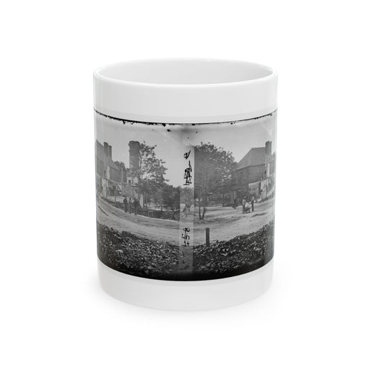 Black-and-white stereo view of a damaged brick building with broken chimneys and small figures on a dirt road.