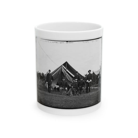 Black and white view of uniformed officers on grass before a wall tent, with stacked rifles nearby.