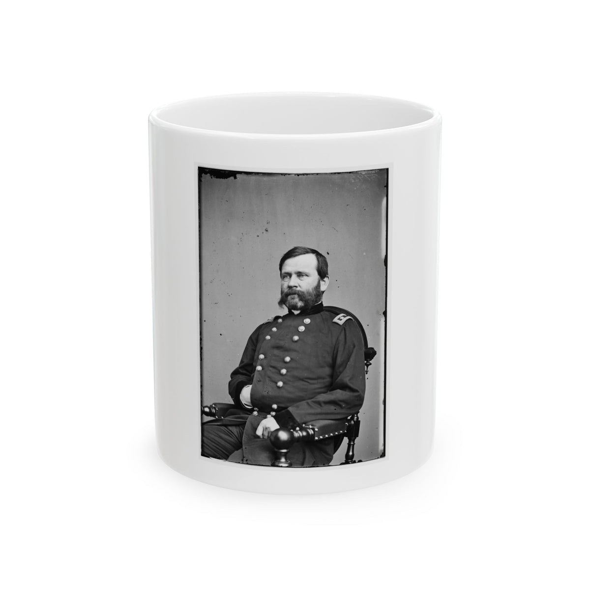 Black and white studio portrait of a seated bearded man in a dark military coat in a wooden armchair.
