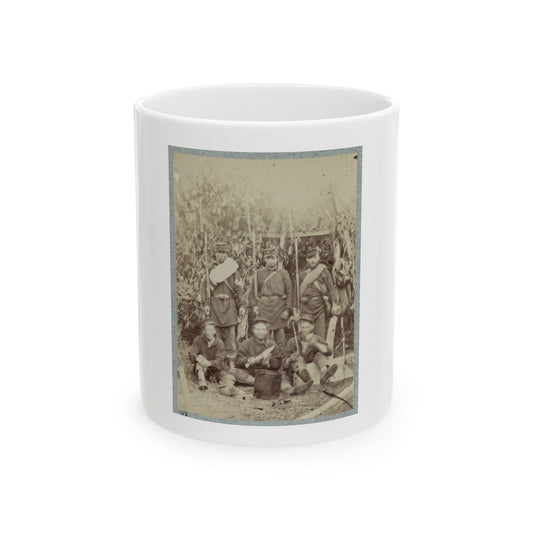 Sepia-toned print of six uniformed soldiers in a leafy camp, three seated around a metal pot and three standing.