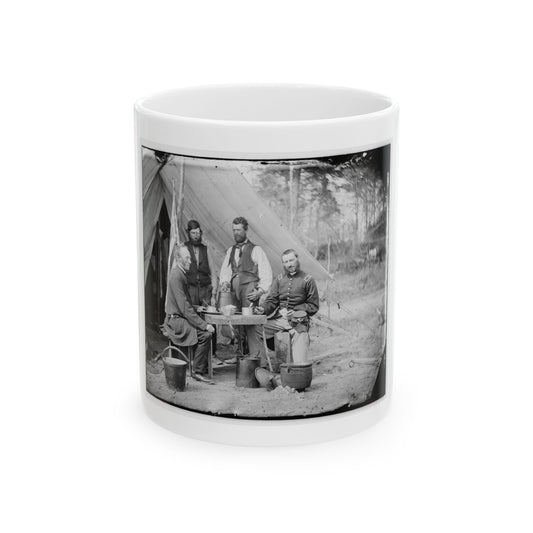 Black-and-white view of four men gathered at a table outside a canvas army tent beside metal kettles.