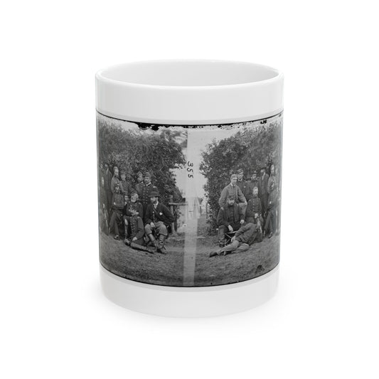 Black-and-white stereo view of uniformed men posed in a group outdoors in front of a leafy shrub.