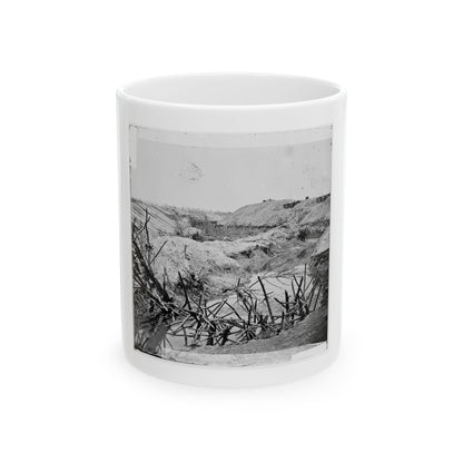 Black and white view of tangled branches in a shallow creek beside dirt embankments and sharpened stakes.