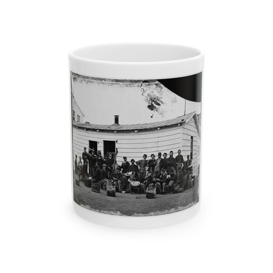 Black and white 1860s view of uniformed musicians with drums, violins and horns before a white clapboard building.
