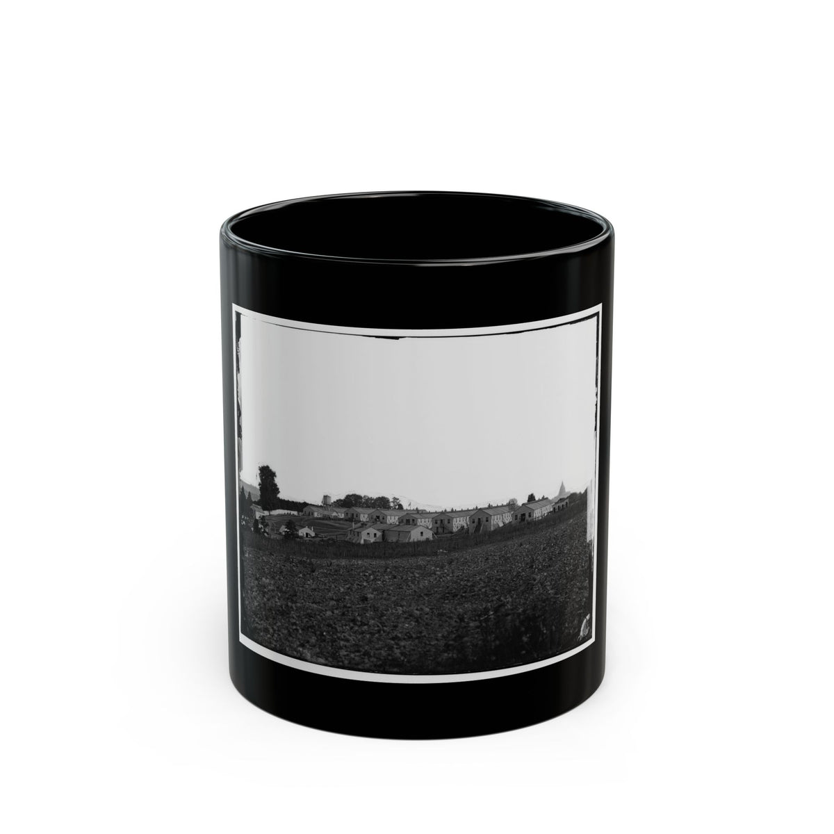 Black and white 1860s view of long wooden barracks on a rise above a ploughed field, with a water tower.