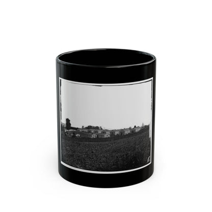Black and white 1860s view of long wooden barracks on a rise above a ploughed field, with a water tower.
