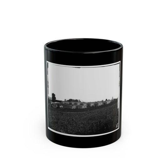 Black and white 1860s view of long wooden barracks on a rise above a ploughed field, with a water tower.