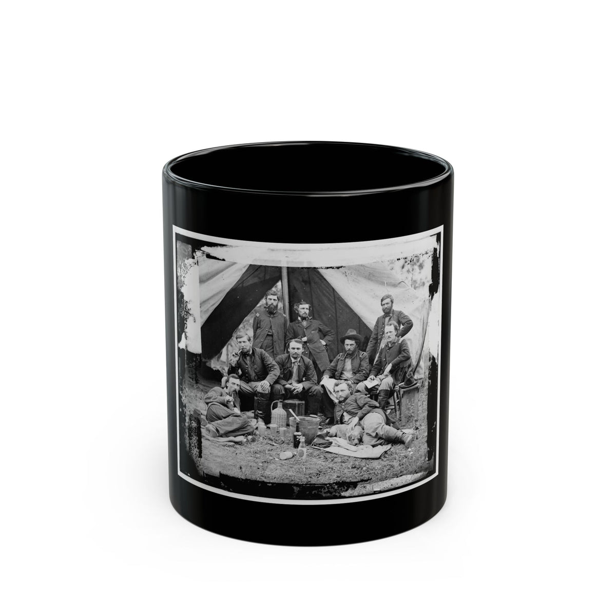 Black and white scene of eight men in military coats posed before a canvas tent, some smoking pipes.