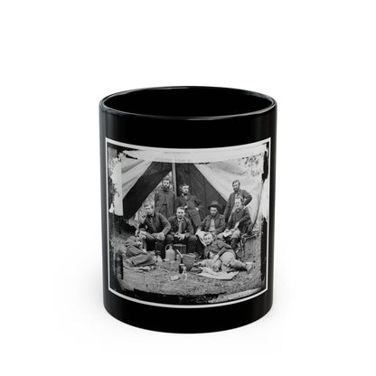 Black and white scene of eight men in military coats posed before a canvas tent, some smoking pipes.