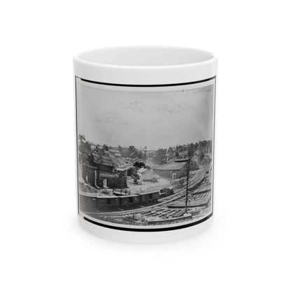 Black and white 19th-century view of a railway yard with boxcars, a brick factory and town buildings on a hillside.