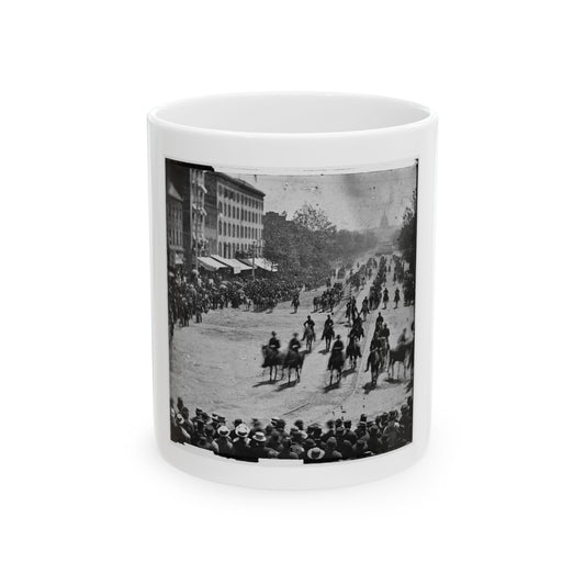 Black and white historical view of mounted cavalry riding down a tree-lined city avenue past a crowd of onlookers.