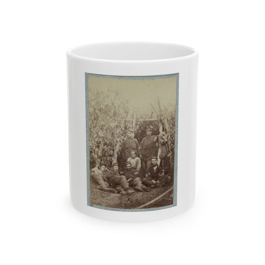 Sepia print showing a group of soldiers in forage caps resting among tall corn stalks in a field.