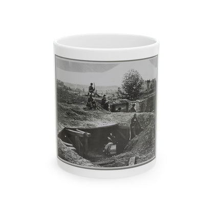 Black and white view of soldiers resting in an earthwork trench beside a timber dugout and sandbag walls.