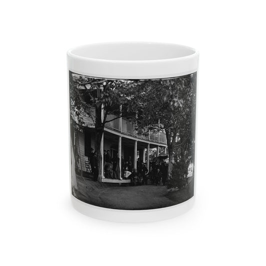 Black and white view of uniformed men gathered on the porch of a two-story wooden building beneath trees.