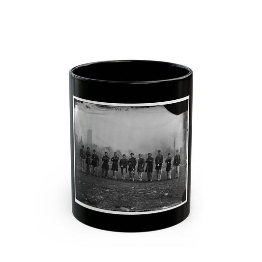Black and white historical view of eleven uniformed men in a line on a grassy lawn, two holding flagstaffs.
