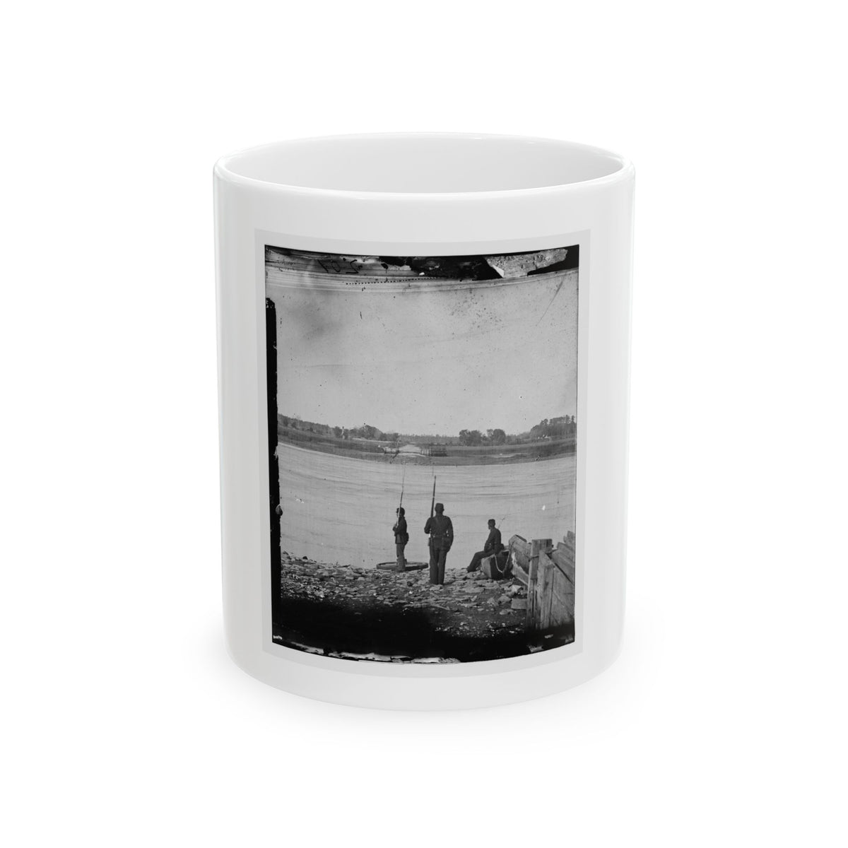 Black and white 1860s scene of two soldiers with rifles and a seated man on a rocky riverbank by a wide river.