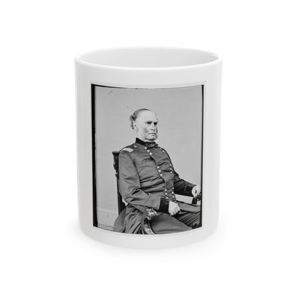 Black and white studio portrait of an older man in a dark button-front coat, seated in a carved wooden chair.