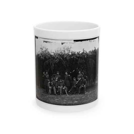 Black and white group portrait of seven uniformed officers, some holding sabres, before a dense drooping tree.