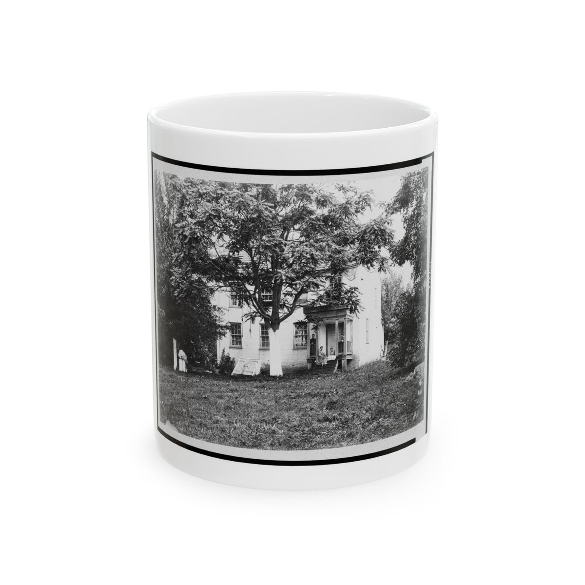 Monochrome late 19th-century scene of a white two-storey house with a porch under a large tree, people on the steps.