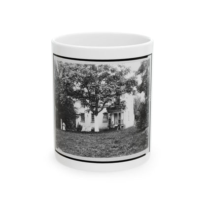 Monochrome late 19th-century scene of a white two-storey house with a porch under a large tree, people on the steps.