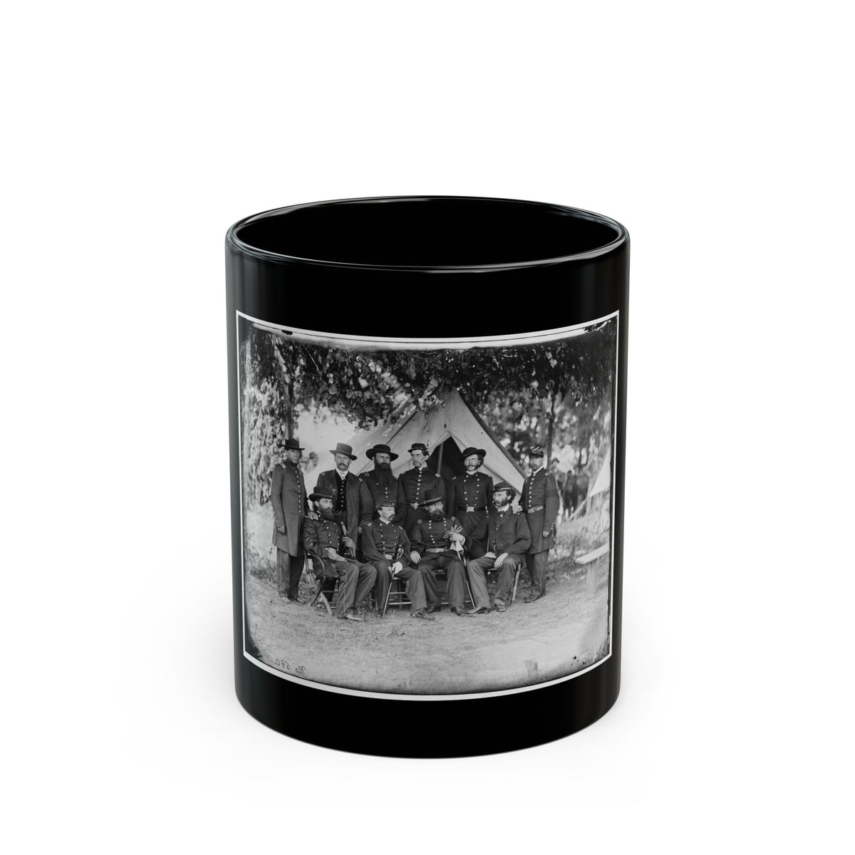 Black and white vintage group portrait of about ten uniformed officers posed before a canvas tent under trees.