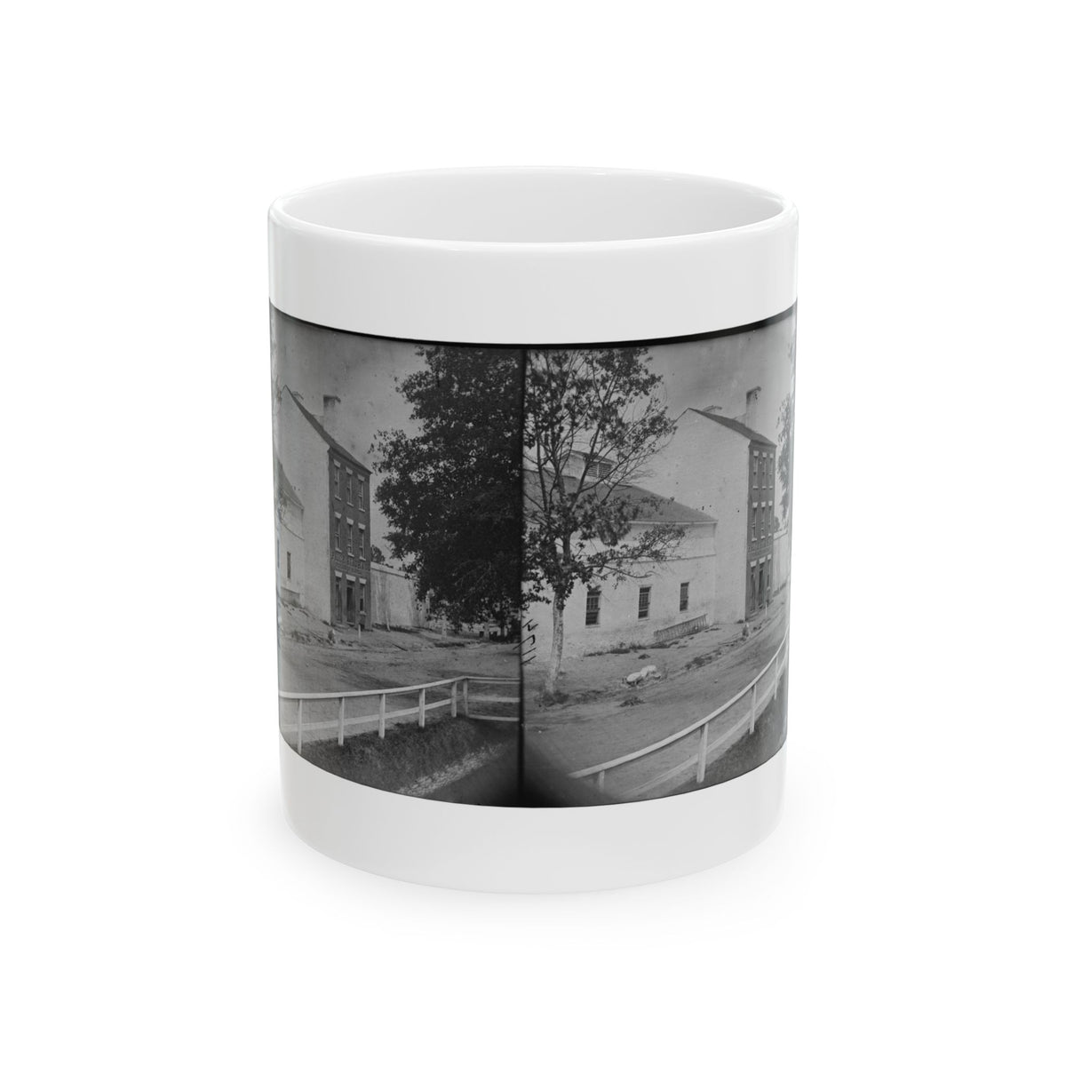 Black-and-white stereograph of whitewashed brick buildings and trees along a dirt street behind a white fence.