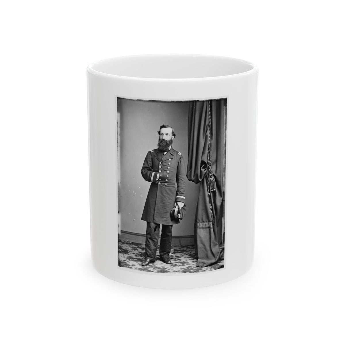 Black and white studio portrait of a bearded officer in a frock coat standing beside a draped curtain.
