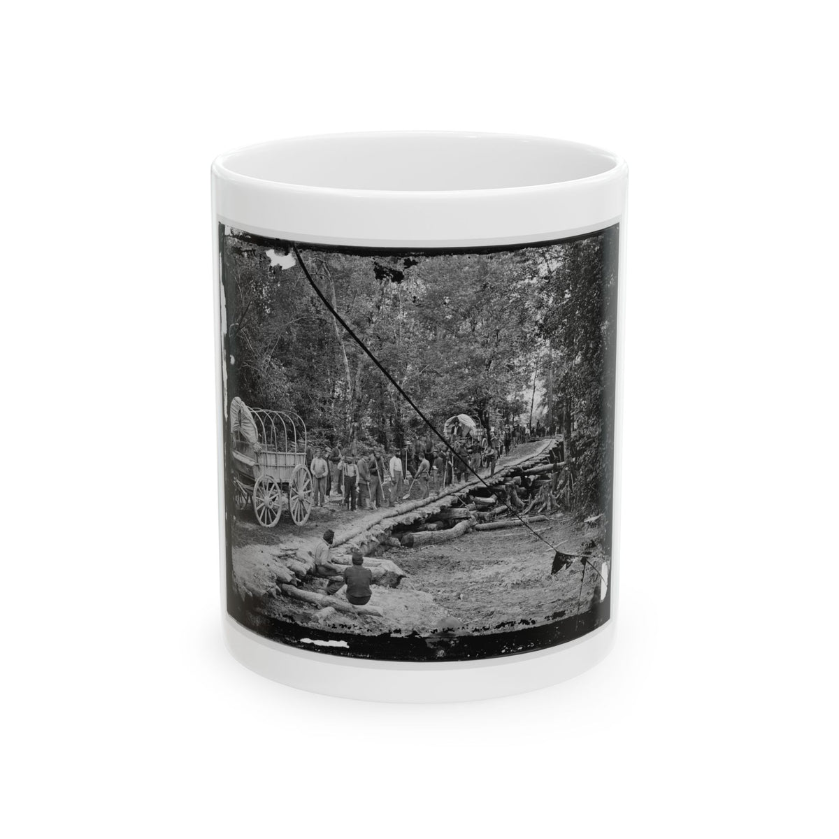 Black-and-white view of covered wagons and workers laying logs to form a corduroy road through a forest.
