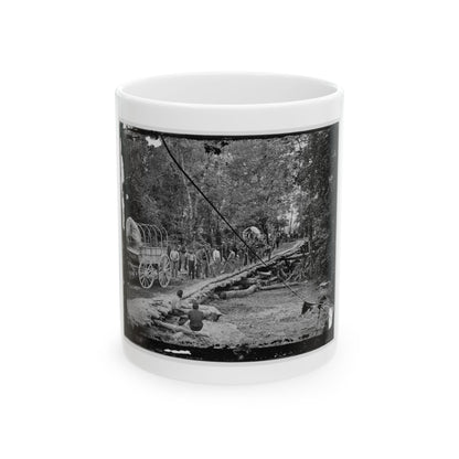 Black-and-white view of covered wagons and workers laying logs to form a corduroy road through a forest.