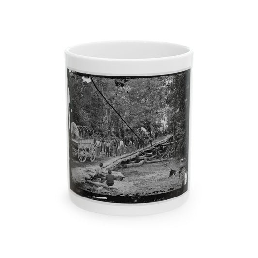 Black-and-white view of covered wagons and workers laying logs to form a corduroy road through a forest.
