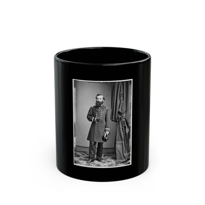 Black and white studio portrait of a bearded officer in a frock coat standing beside a draped curtain.