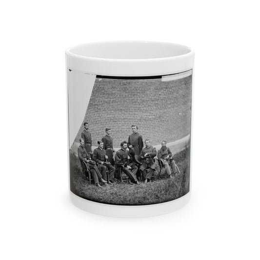 Black and white 1860s group portrait of seven uniformed officers posed on grass before a brick wall.