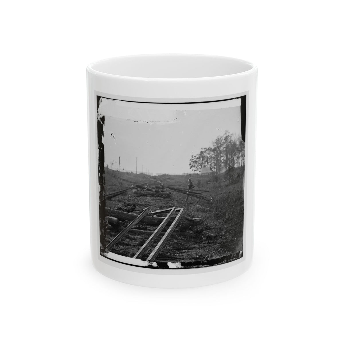Black and white view of bent rails lying across wooden ties in an open field, with a lone figure in the distance.