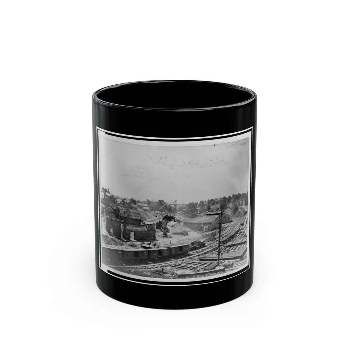 Black and white 19th-century view of a railway yard with boxcars, a brick factory and town buildings on a hillside.
