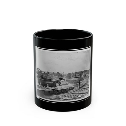 Black and white 19th-century view of a railway yard with boxcars, a brick factory and town buildings on a hillside.