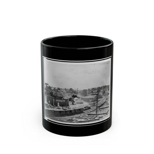 Black and white 19th-century view of a railway yard with boxcars, a brick factory and town buildings on a hillside.
