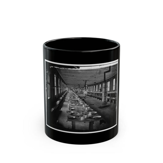 Black and white historical view of a long wooden mess hall, with tables set for a meal and a large ornate stove.