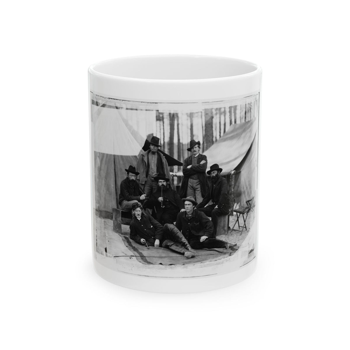 Black-and-white albumen view of seven men in coats, some smoking pipes, posed before canvas tents among pines.