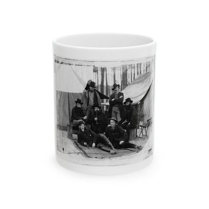 Black-and-white albumen view of seven men in coats, some smoking pipes, posed before canvas tents among pines.