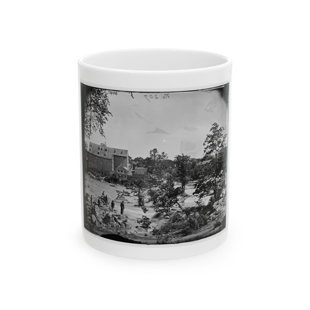 Black-and-white view of a brick mill and waterwheel beside rapids, with men standing on rocks in the stream.