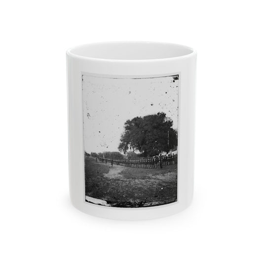 Black-and-white 1860s view of a long line of uniformed soldiers across a field beside an oak tree.