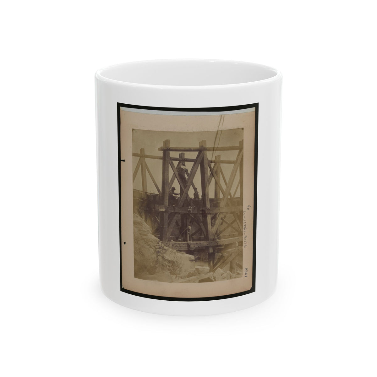 Sepia scene of workmen on a timber trestle frame with cross bracing above rough rocks.