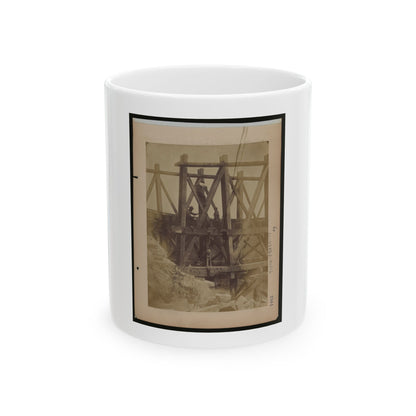 Sepia scene of workmen on a timber trestle frame with cross bracing above rough rocks.