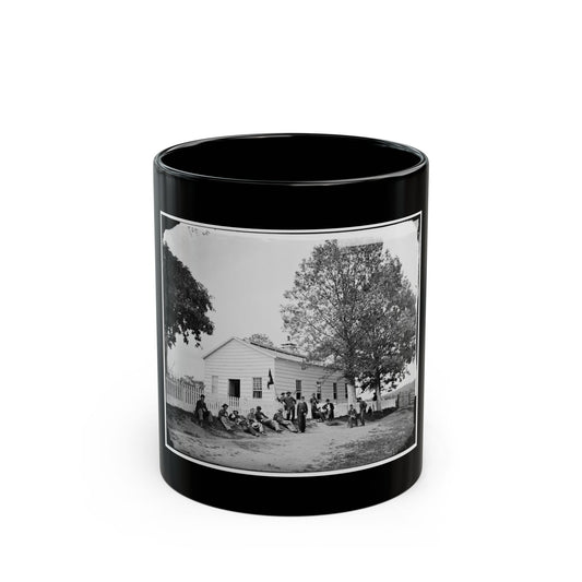 Black and white 19th-century view of men resting outside a white clapboard house beside a picket fence and tree.