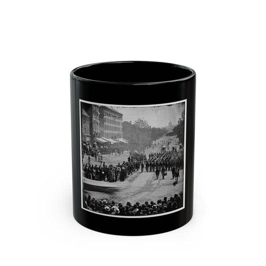 Black and white 19th-century view of a column of soldiers with rifles marching down a city avenue past crowds.