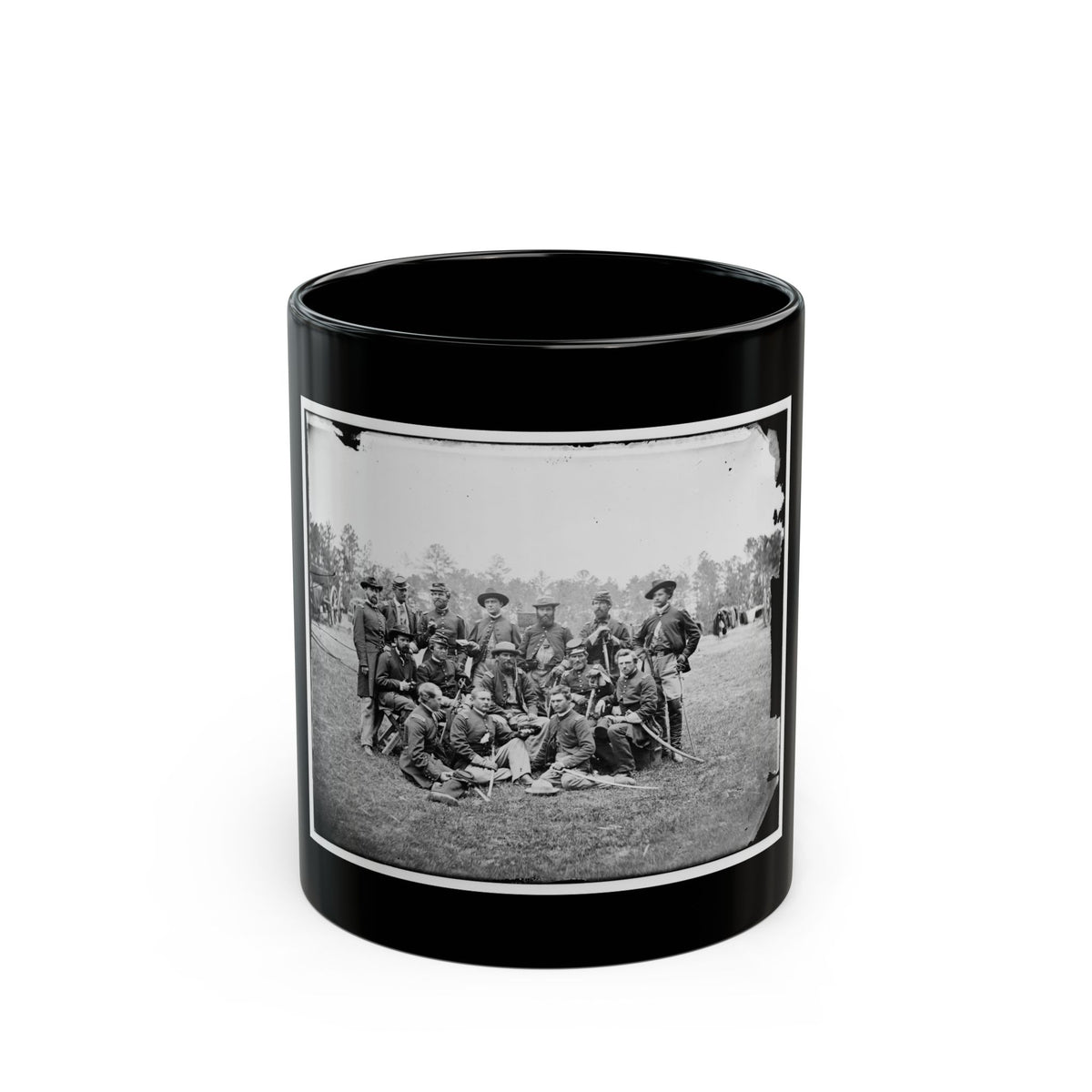 Black and white group portrait of about fourteen uniformed men with sabers posed on a grassy field before trees.