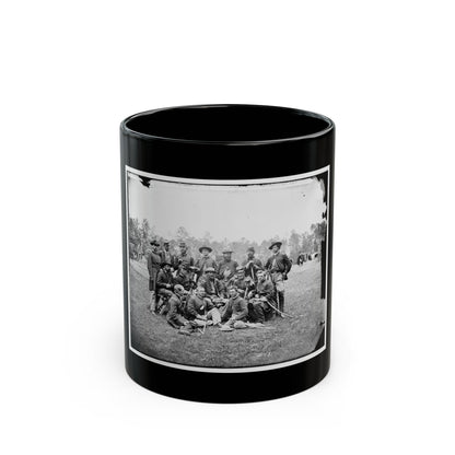 Black and white group portrait of about fourteen uniformed men with sabers posed on a grassy field before trees.