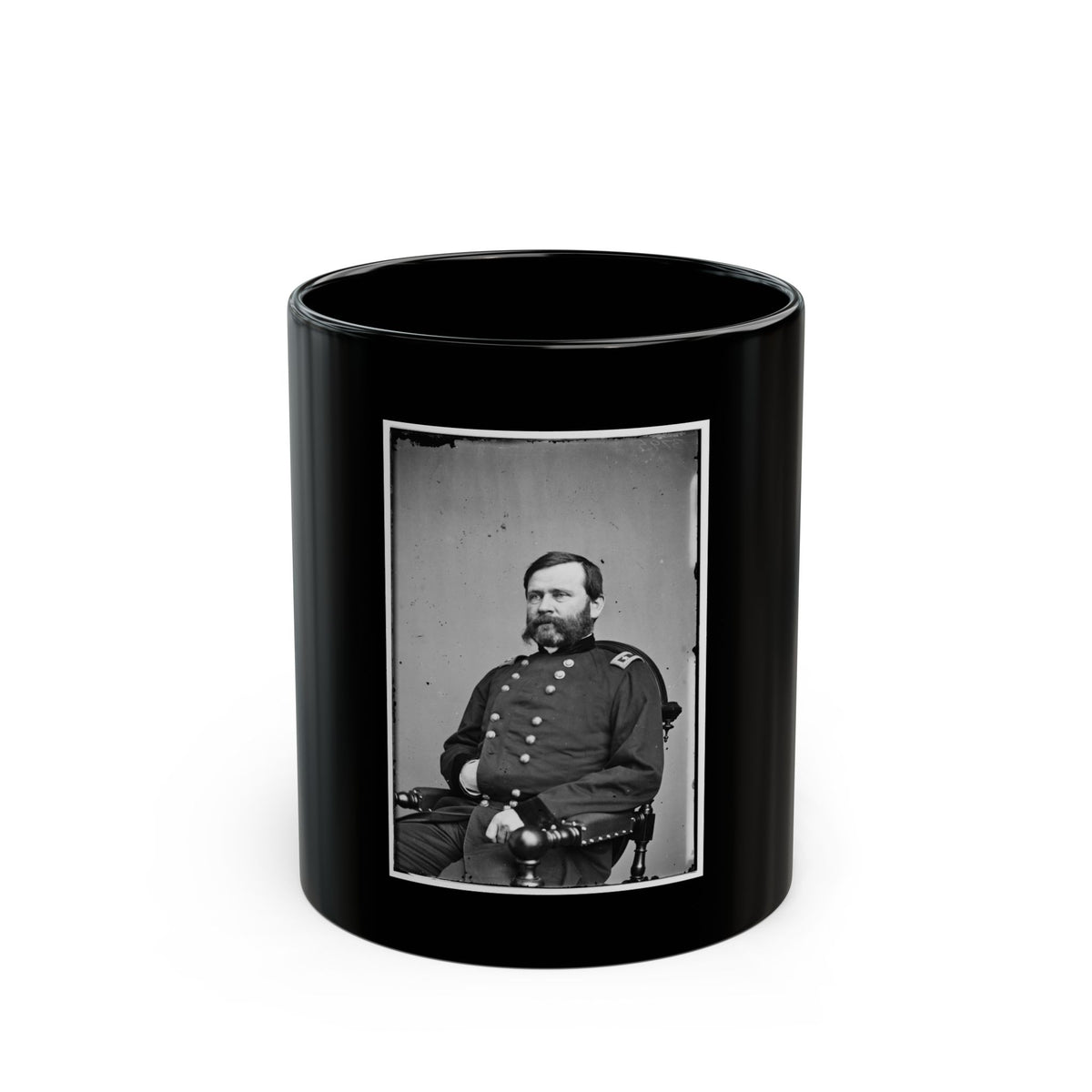 Black and white studio portrait of a seated bearded man in a dark military coat in a wooden armchair.