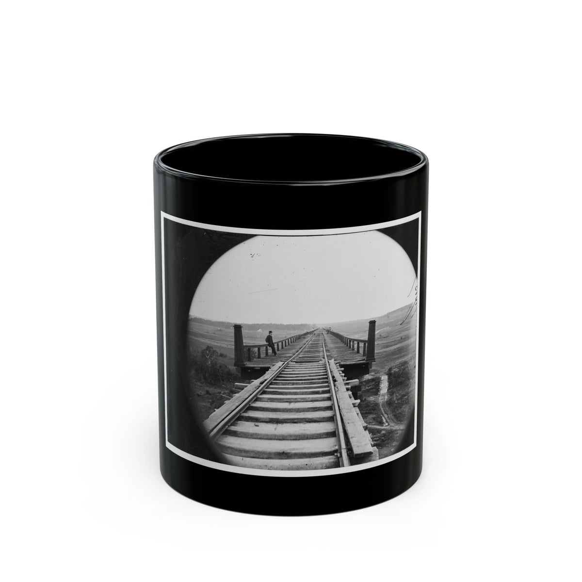 Black and white view of a long wooden railway trestle with a man in a top hat standing at its railing.