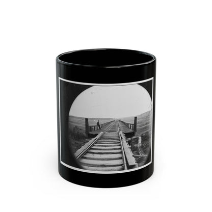 Black and white view of a long wooden railway trestle with a man in a top hat standing at its railing.